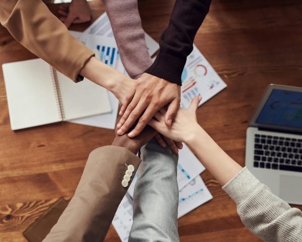 Diverse professionals unite for teamwork around a wooden table with laptops and documents.