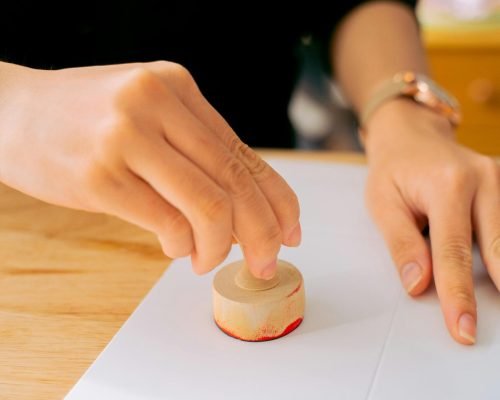 Close-up of a person using a wooden stamp on white paper indoors.
